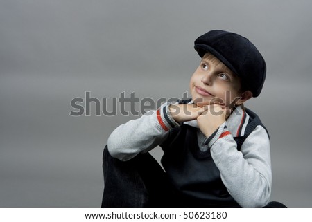 cute boy in old school cap sitting with hands crossed in front and smiling with natural nice smile isolated over gray background