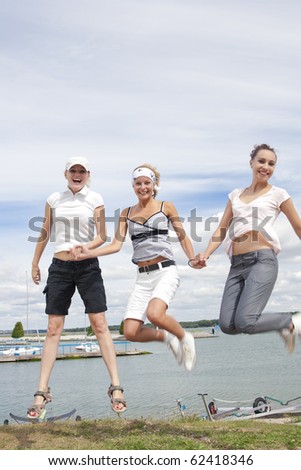 three nice and youn caucasian girls jumping out together over the hill in front of water line in yacht club and having fun together
