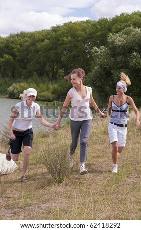 young caucasian pretty girls running on the road near forest and in front of waterline and having fun together
