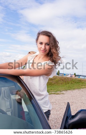 young pretty and beautiful caucasian dark hair girl standing near car with calm nice facial expression and waiting. shoot made on location with strobes