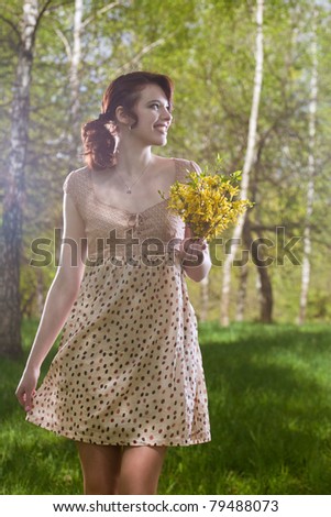 young and pretty caucasian brunette girl standing outside in green forest and holding bunch of flowers- outside. shot made with strobes on location
