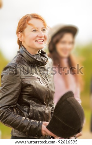 smiling equestrian red haired girl with jockey helmet before riding standing outside