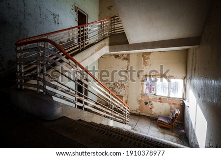 Abandoned building creepy dark moody staircase in dilapidated run down old deserted hospital school ruin with a single empty chair indoors on stairs landing no one there Photo stock © 