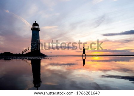 Lighthouse standing in pool of water stunning sunset reflection reflected in sea water. Single lone man exploring north Wales seashore sand beach still water orange glow sunrise golden hour blue hour. Stockfoto © 