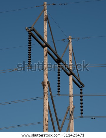Electric power lines mounted on insulators and a tall wood power pole.  These wire transfer electrical energy to households and industry.