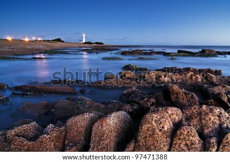 night long exposure image of coastline with rocks on the first plane and a lighthouse on the horizon