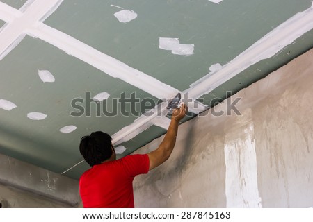 Worker using gypsum plaster ceiling joints.
