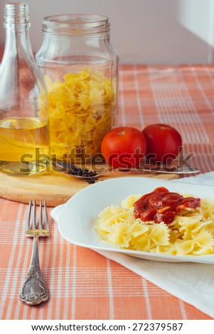 Farfalle with tomato sauce on white dish, olive oil bottle, jar and raw tomatoes vertical selective focus