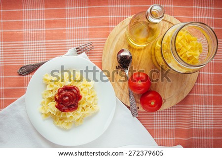 Farfalle with tomato sauce on white dish, olive oil bottle, jar and raw tomatoes top view selective focus
