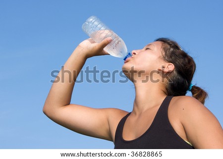 Young athlete drinks water from a clear plastic bottle after a running exercise at an outdoor track.