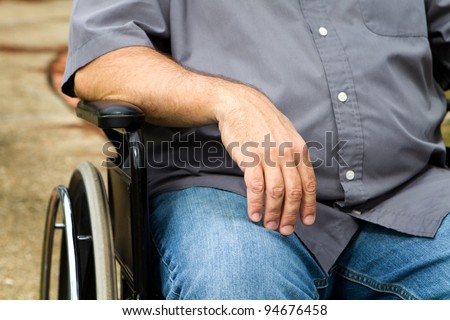 Close up of disabled man\'s arm and torso as he sits in a wheelchair.