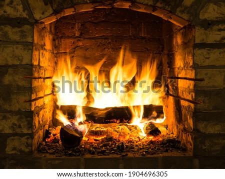 Burning firewood in fire-box of fireplace in country cottage. Rustic cooking oven with burning logs.