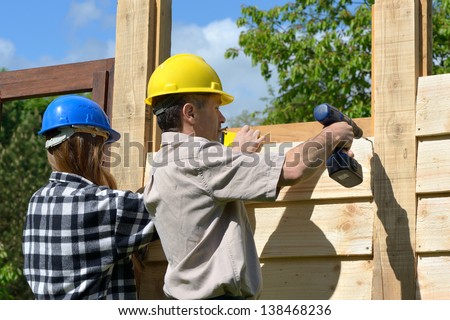 Both male and female workers who are building a wooden chalet