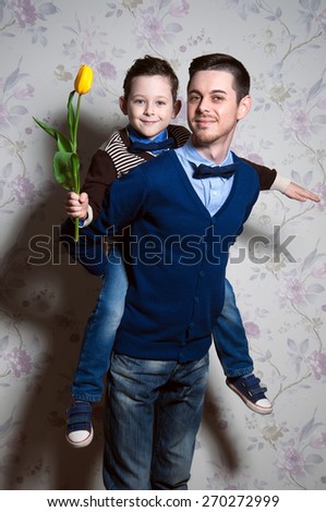 young father and his cute son with yellow flower in his little hand. happy blue-eyed kid. man which is proud of the son