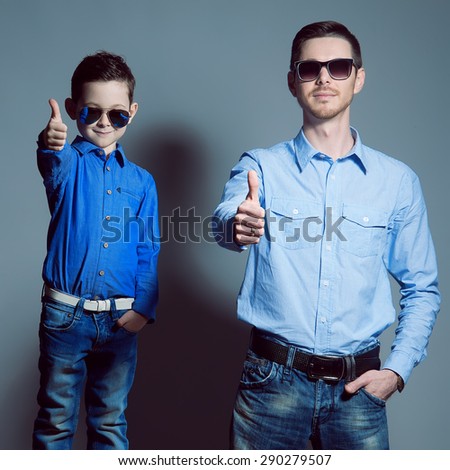 Two gentlemen: young father and his little cute son in sunglasses. Are dressed in shirts and jeans. Studio shot