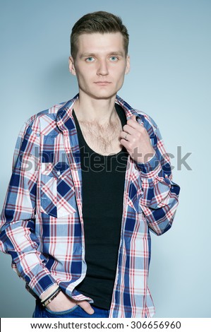 Portrait of young man with very handsome face in shirt and jeans with stylish haircut posing over grey background. Perfect skin & hair. Studio shot