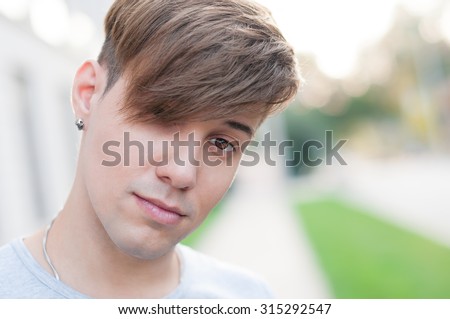 Portrait of young dark-eyed  man, outdoors. He is wearing a ear-ring. Hipster style.