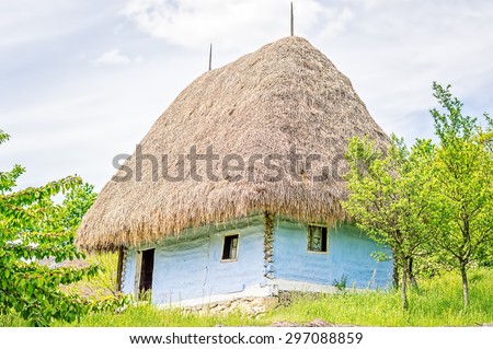 Light blue old clay house with a thatched roof, exposed wooden beams and stone foundation.