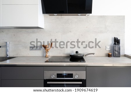 Kitchen with built in appliance, electric cooker hood, stove, oven and sink. Frying pan on glass ceramic surface at marble countertop close to wooden spoons and knives, under white cupboards Сток-фото © 