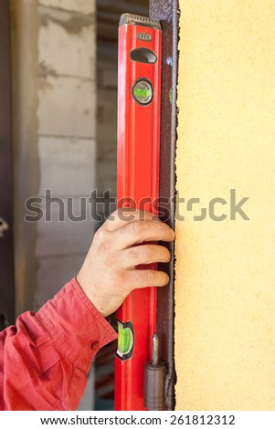 Builder ensuring that a door is vertical holding a builders level against the door as he installs it on a new building during construction