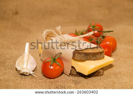 Sandwich with cheese wrapped in paper, cherry tomatoes and garlic on old cloth