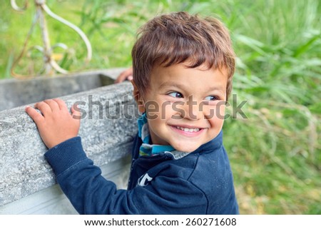 Child with his hands clinging to a well turns to watch his friends smiling