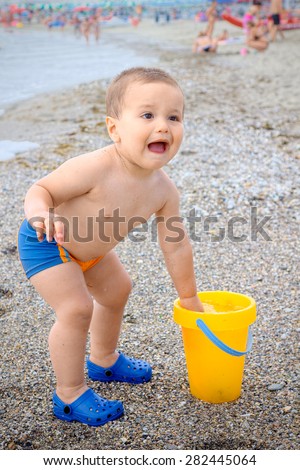 Child two year old on the beach starts crying because he dipped his hand in the water too cold bucket that filled