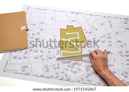 Town planning and land use planning - hand holding a measuring ruler in front of a zoning of plots, on a cadastral plan placed on a desk Imagine de stoc © 