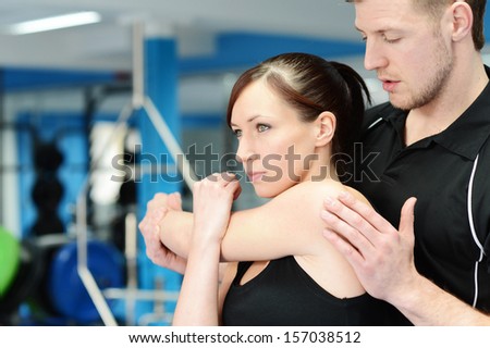 Personal trainer helping young woman in gym with stretching exercises