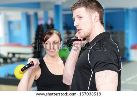 Young woman working out with kettle bell weights, with personal trainer in gym