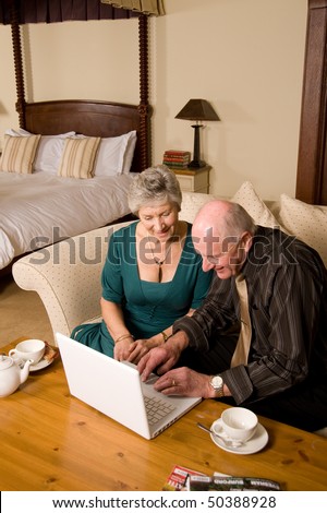 Happy senior couple using laptop in luxurious hotel bedroom suite