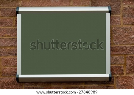 a blank green texture public notice board, hanging on a red stone wall.