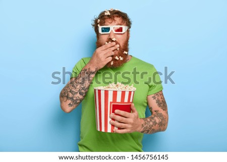 Shot of attractive ginger guy swallows fresh popcorn in cinema while watches exciting movie, wears three dimension glasses and casual green t shirt, all attention at screen, being attentive spectator Photo stock © 