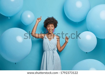 Upbeat cheerful festive woman with hollywood smile, laughs out of joy, moves carefree and dances to music, has fun, makes happy holiday photo, celebrates anniversary, surrounded by balloons.