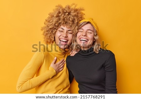 Sincere human emotions concept. Positive overjoyed young women have fun laugh gladfully smile toothily cannot stop laughing stand closely to each other dressed casually isolated over yellow wall Сток-фото © 