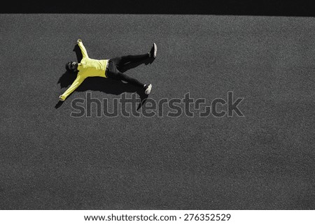 Top view runner in yellow sportswear resting lying on a black asphalt after running. Jogging man taking a break during training outdoors. Caucasian fitness model 20s in Barcelona, Spain.