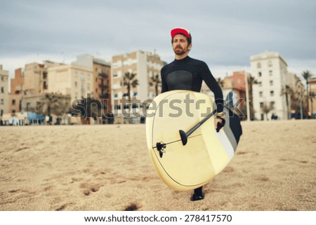 Young surfer sports man wearing surfing neoprene waterproof suits and carrying his surfing board on a white sand beach
