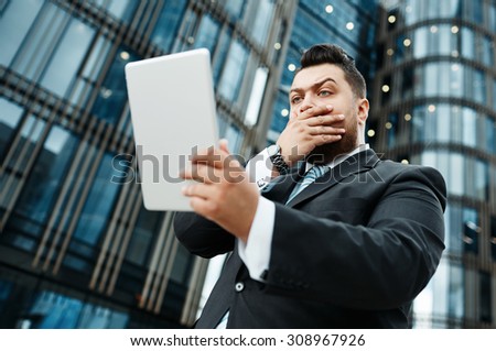 Portrait of handsome surprised business man reads news on tablet while standing in city financial street, business man reading messages, stylish man using internet outdoors.