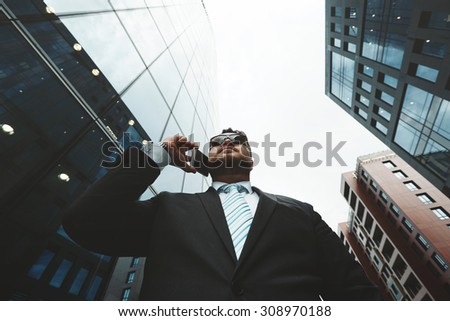 Bottom view portrait of successful business man talking on smart phone outside office. Attractive adult man in suit talking on the phone and standing near his financial office  background