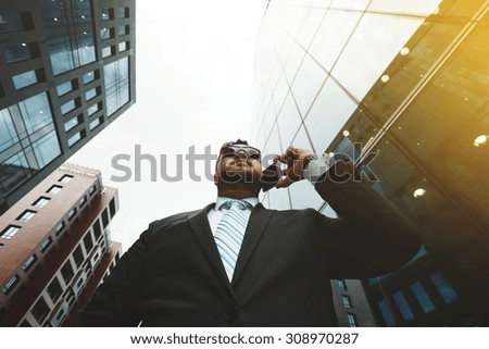 Bottom view portrait of successful business man talking on smart phone outside office. Attractive adult man in suit talking on phone and standing near his financial office  background, flare light