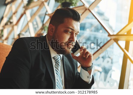 Portrait of successful business man talking on smart phone inside coffee shop. Attractive adult man in suit talking on the phone, flare light