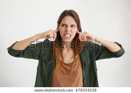 Agressive female plugging her ears being angry with her neighbours who are very noisy. Irritated beautiful young woman trying to avoide loud sounds from house next door hating creaking sounds Foto d'archivio © 