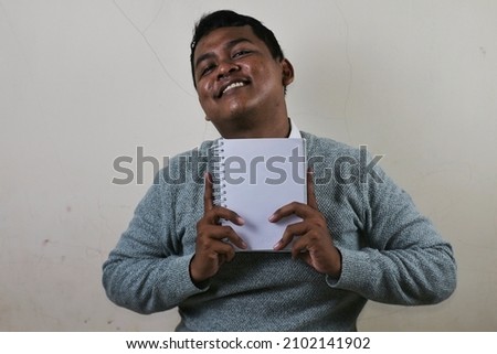 a young asian man holding a white book or binder with both hands and placing it in front of his chest while smiling and looking happy Foto stock © 
