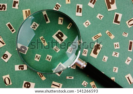 letters cut from newspaper and magnifying glass on green background