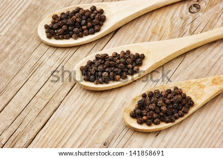 Black pepper in wooden spoon on the old board