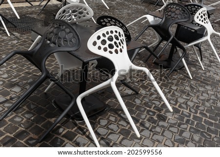Black and white plastic chairs in a street cafe after rain in Italy