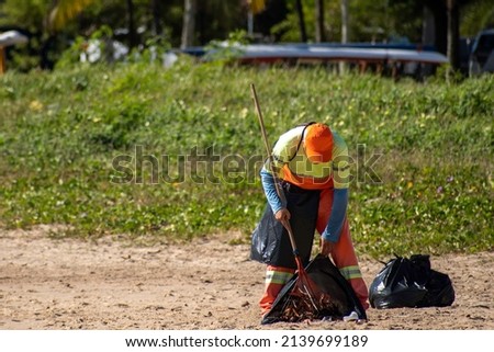 Gari cleaning the beach sand using a rake. Man throws dirt into garbage bag Stock fotó © 