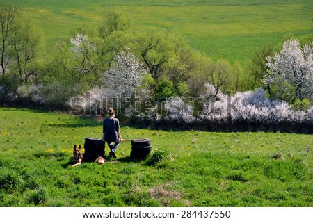 Friendship between young girl and her dog on beautiful spring meadow, where girl sitting in calm atmosphere