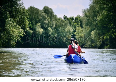 Two friends in canoe are swimming on the river between beautiful green forest