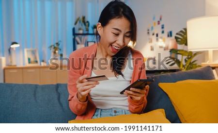 Night time beautiful smiling asian lady use cellphone order online shopping product with credit card on sofa in living room. Stay at home, Self quarantine activity, Fun activity for covid quarantine.
